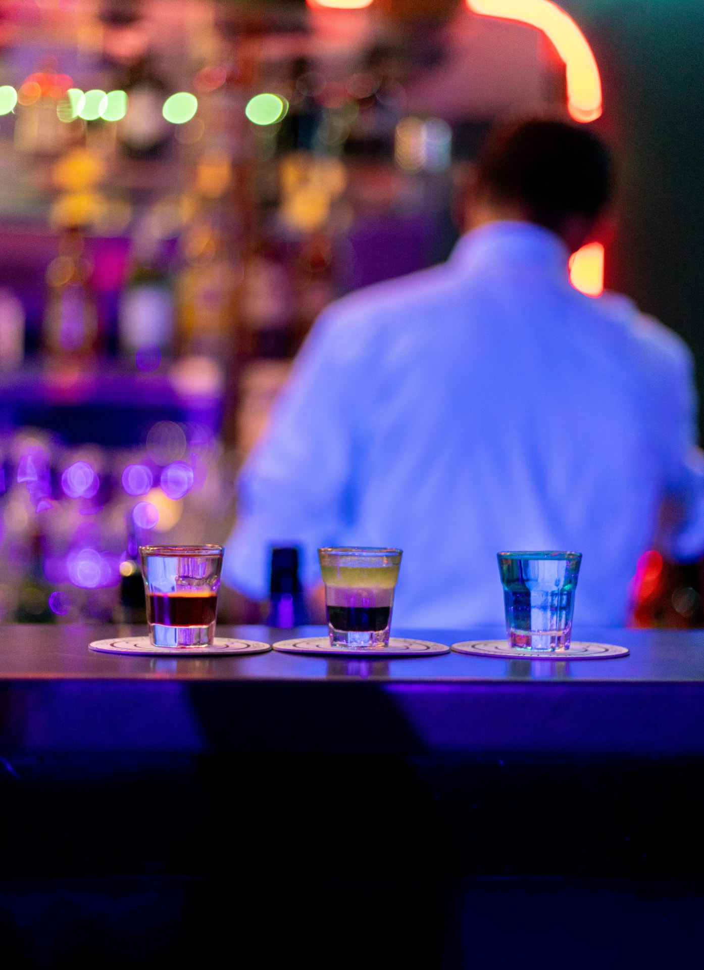 Colorful shots lined up on a bar with vibrant nightlife lights in the background