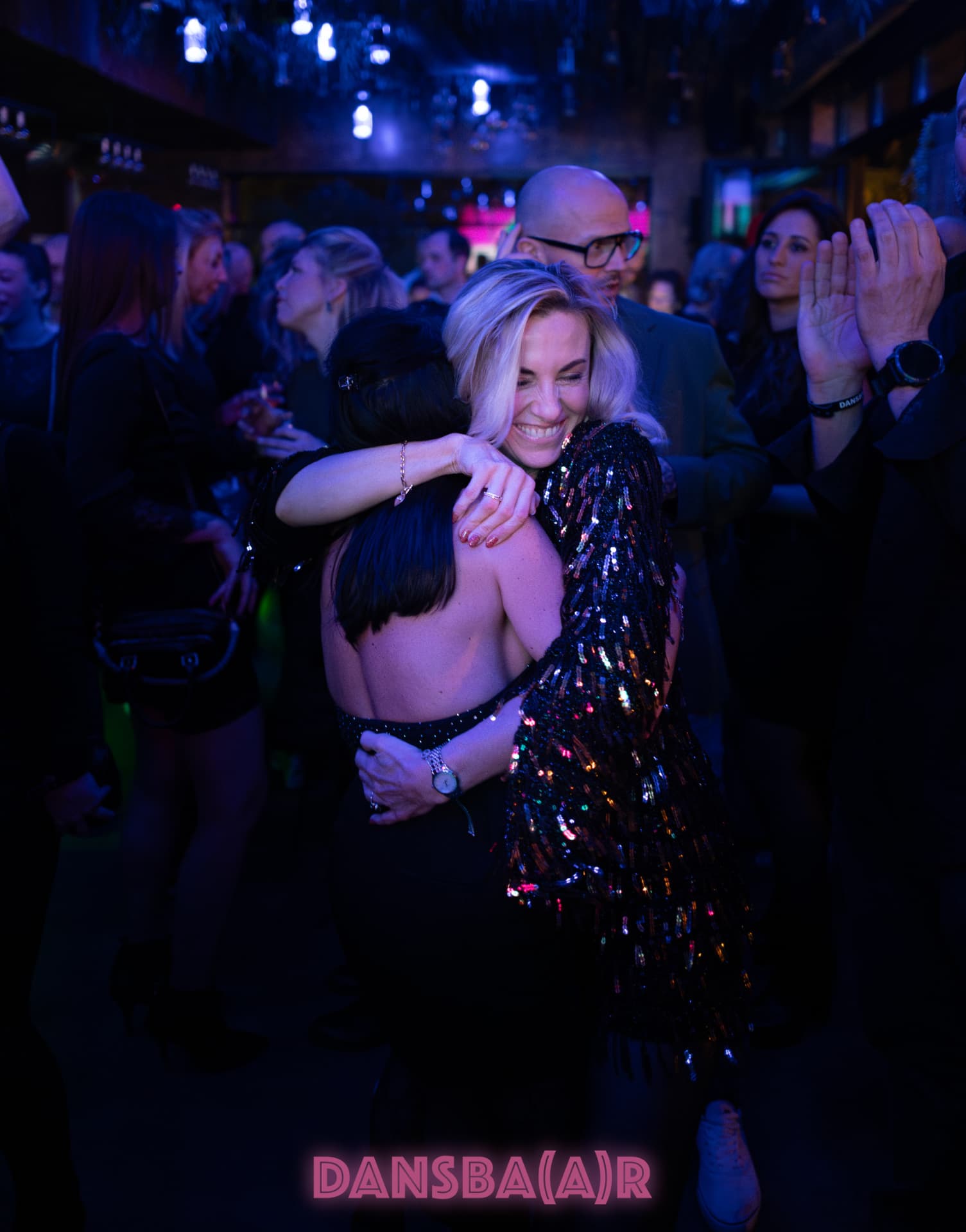 Two guests hugging on a packed nightclub dance floor under blue lights